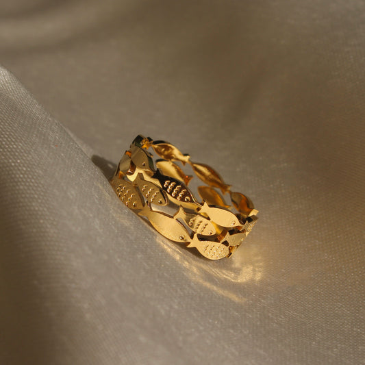 Adjustable gold fish ring on a neutral background