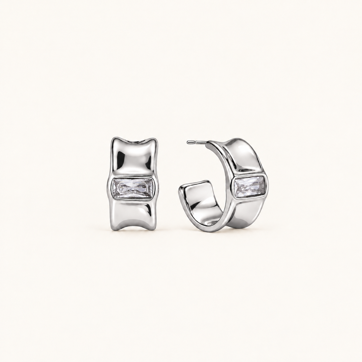 Celeste polished silver hoop earrings with sculpted edges and rectangular clear stones on a pale beige background.