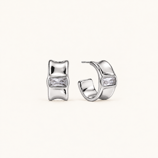 Celeste polished silver hoop earrings with sculpted edges and rectangular clear stones on a pale beige background.