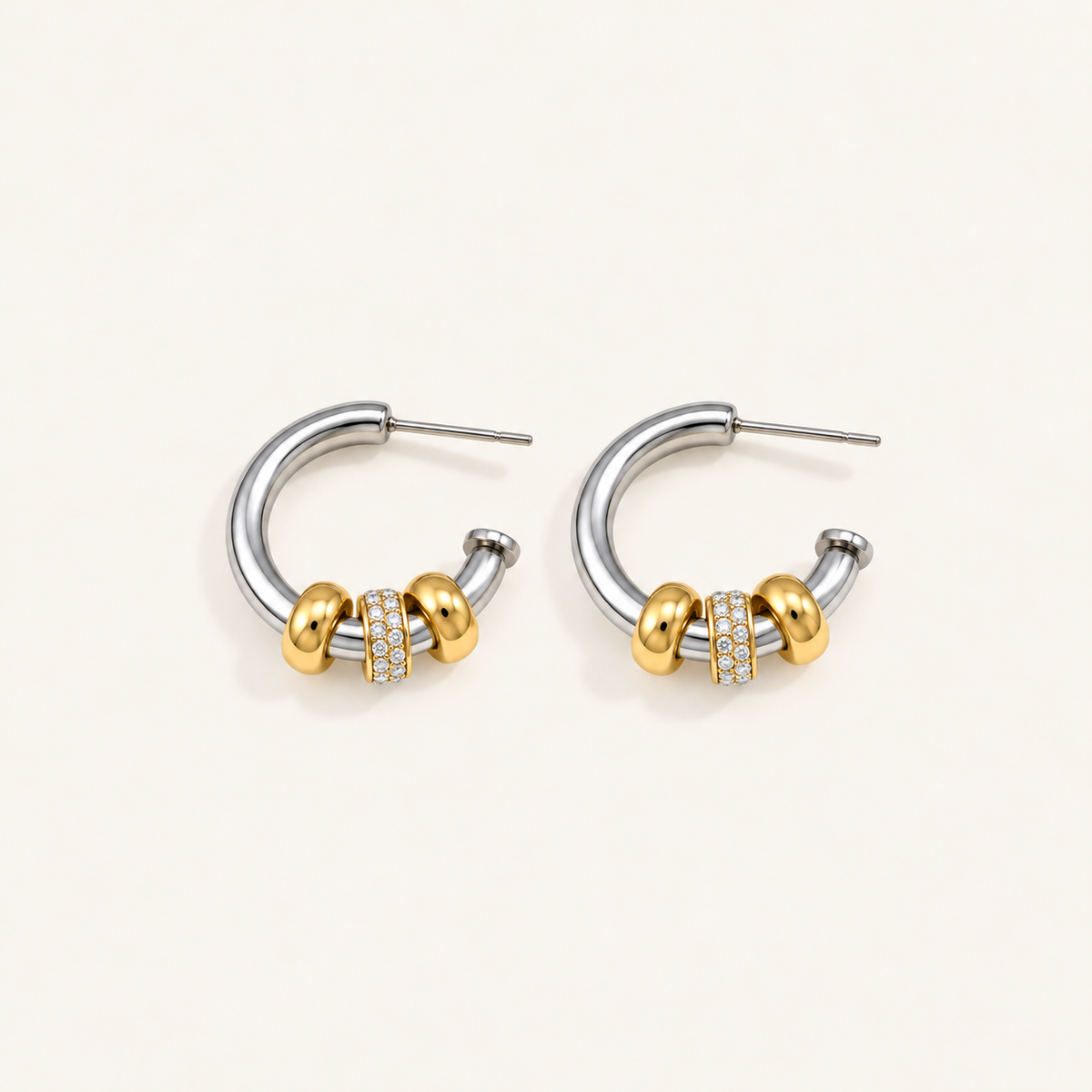 Pair of waterproof silver hoop earrings with gold beads and a crystal pavé band on a pale beige background.