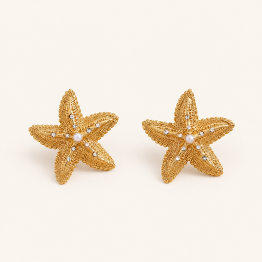 A pair of gold starfish-shaped stud earrings with small clear rhinestones and a central white pearl, displayed on a clean off-white background.