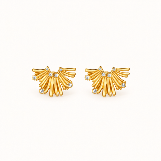 A pair of gold wing-shaped stud earrings with small clear gemstones, displayed on a clean off-white background. Gold floral statement earrings with sparkling crystal accents on a neutral background.