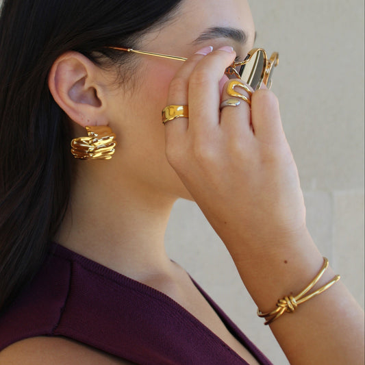 Person wearing gold hoop earrings and rings with a neutral background